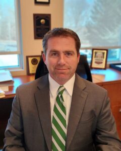 man sitting at a desk wearing a green striped tie and suit.